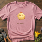 Pink t-shirt with a cartoon chicken and 'F-CAW-F' text on a wooden surface with flowers and scissors.