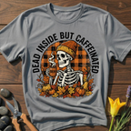Gray t-shirt with a skeleton design holding a coffee cup, surrounded by pumpkins and leaves on a wooden surface.