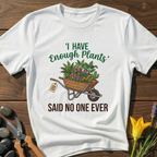 White t-shirt with gardening graphic and text on a wooden surface with gardening tools and flowers.